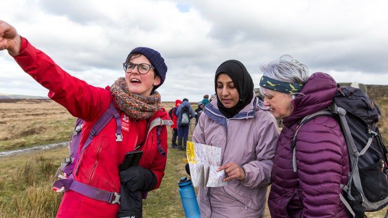Three women, one in red is pointing at something whilst the other two look at a map